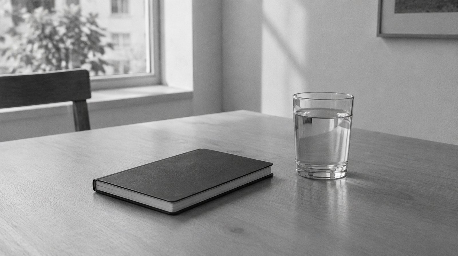 KI-generierte Darstellung: geschlossenes Notizbuch und ein Glas Wasser auf einem schlichten Tisch