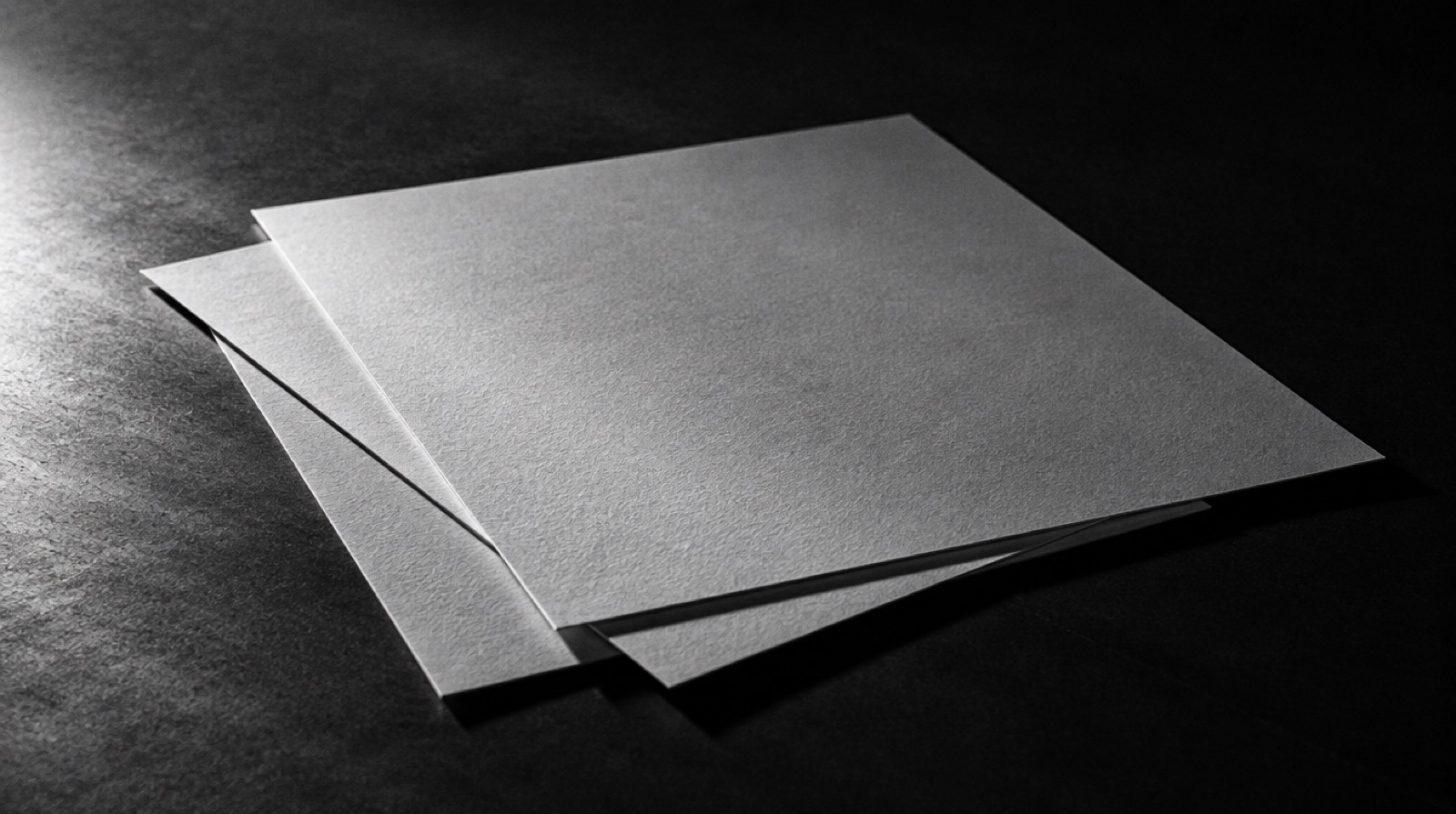 KI-generierte Darstellung: zwei leere Blätter Papier auf dunkler Tischplatte im Streiflicht